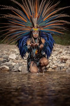 a woman with feathers on her head kneeling in the water