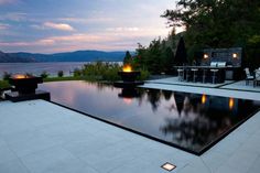 a large pool surrounded by lounge chairs next to a lake at dusk with the sun setting