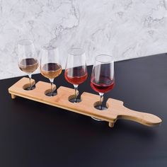 four glasses of wine are on a wooden tray with a marble wall in the background