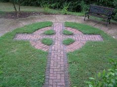 a cross made out of bricks in the middle of a yard with a bench behind it