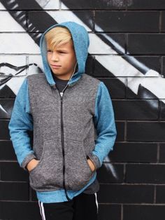 a young boy standing in front of a graffiti wall wearing a hoodie and sweatpants