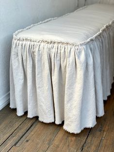 a white bed with ruffled bedskirt on the bottom and sides, in front of a wall