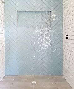 a bathroom with white tile and blue glass shower door in the center, along with two black handles