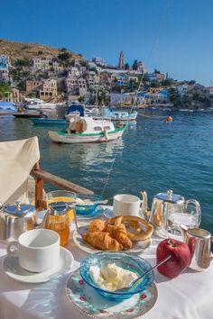 a table that has some food on it near the water with boats in the background