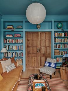 a living room filled with furniture and bookshelves next to a wooden door in front of a blue wall