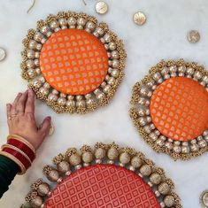 two orange and gold decorative pieces on a table with other items around them, including a woman's hand