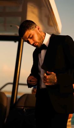 a man in a tuxedo standing next to a boat with his head down