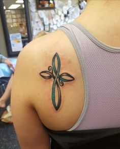 a cross tattoo on the back of a woman's upper arm, with an aqua green ribbon