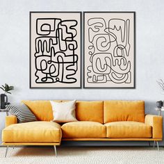 two black and white paintings on the wall above a yellow couch in a living room