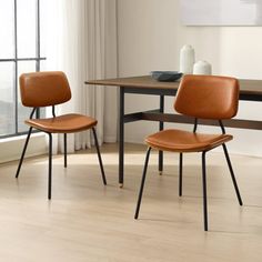 two brown chairs sitting next to each other in front of a table with a vase on it