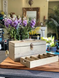 a wooden box sitting on top of a counter next to purple flowers and a mirror