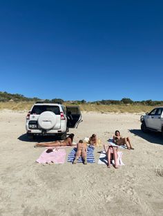 three people are sitting in the sand near their cars