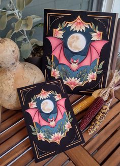 two greeting cards sitting on top of a wooden table next to corn and a potted plant