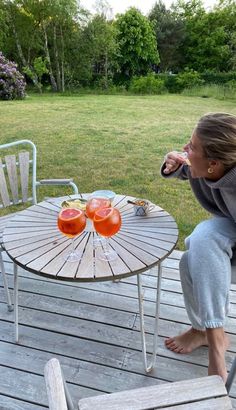 a woman sitting at a table with two glasses of orange juice on top of it