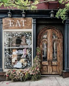 a store front with flowers in the foreground and an open door on the other side