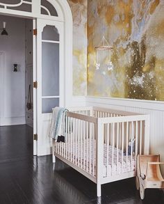 a baby's crib in front of a wall with gold and white paint