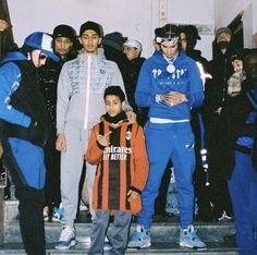 a group of young men standing next to each other in front of a staircase with people