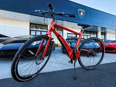 a red bike parked in front of a car dealership with other cars behind it