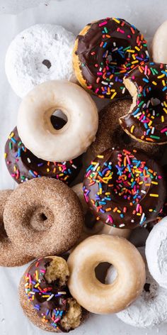 a bunch of doughnuts that are on top of a white paper bag with chocolate frosting and sprinkles