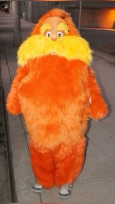 a man in an orange and yellow costume standing on the sidewalk with his hands behind his back