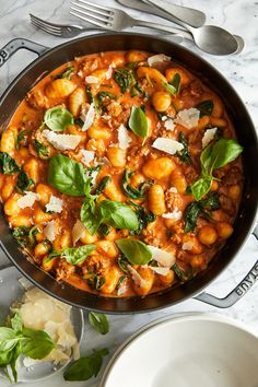 a skillet filled with pasta and spinach on top of a marble countertop