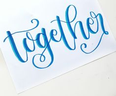 the word together written in blue ink on a white paper with a pen next to it