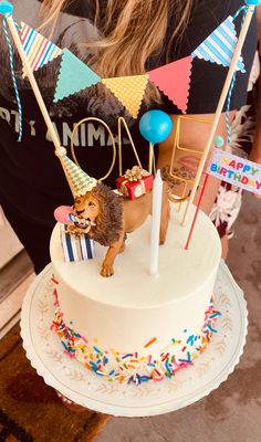 a small dog is on top of a birthday cake with flags and streamers around it