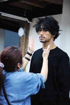 a man with black hair standing next to a woman who is holding her hand out