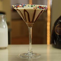 a glass filled with chocolate and sprinkles next to a bottle of milk