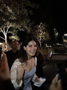 a woman standing next to a group of people holding cell phones in her hands at night