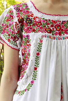 a woman wearing a white dress with red and green flowers on it's chest