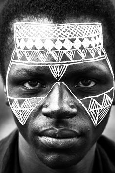 a man with white face paint on his face and black hair is looking at the camera