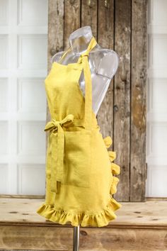 a yellow apron with ruffles is on display in front of a wooden wall