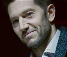 a close up of a person wearing a suit and tie with a beard smiling at the camera