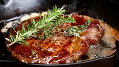 some meat is cooking in a skillet with herbs on top, and potatoes to the side