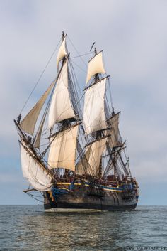 an old sailing ship in the middle of the ocean with white sails and two masts