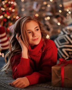 a woman laying on the floor next to a christmas tree with presents in front of her