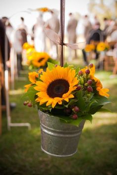 sunflowers are hanging from a metal bucket at an outdoor wedding ceremony with other people in the background