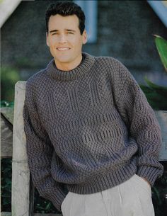 a man wearing a gray sweater and khaki pants sitting on a wooden bench