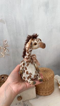 a stuffed giraffe sitting on top of a basket next to a person's hand