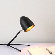 a desk lamp sitting on top of a table next to an open book and pen