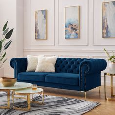 a living room with blue velvet couches and gold coffee table in front of paintings on the wall