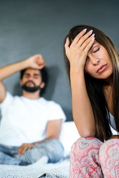 a man and woman sitting on a bed with their hands to their foreheads as they look at each other