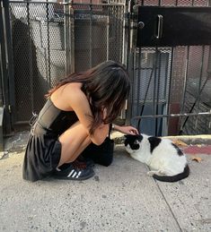 a woman petting a black and white cat on the sidewalk next to a fence