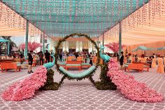 an outdoor event with pink flowers on the ground and blue canopy over tables in the background