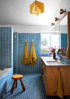 a blue tiled bathroom with yellow towels hanging on the wall and wooden stool in front