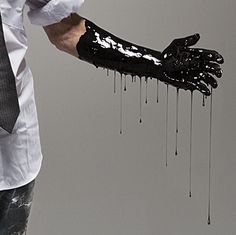 a man in white shirt and tie with black paint dripping on his arm holding up a glove