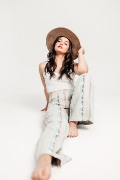 a woman sitting on the ground with her legs crossed and wearing a wide brimmed hat