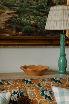 a green lamp sitting on top of a wooden table next to a bowl and pillow