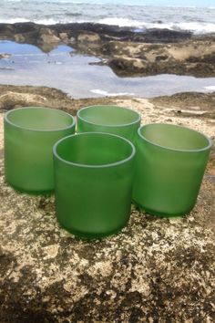 four green cups sitting on top of a rock near the ocean